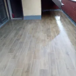 Błyszcząca, drewnopodobna terakota ułożona na balkonie z widocznym odpływem wody, świeżo po umyciu.