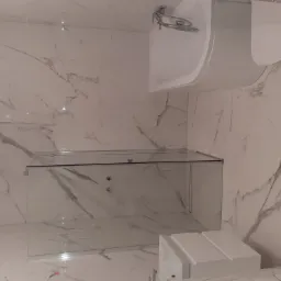 Nowoczesna łazienka z marmurowymi płytkami, szklaną kabiną prysznicową i podwieszaną toaletą.