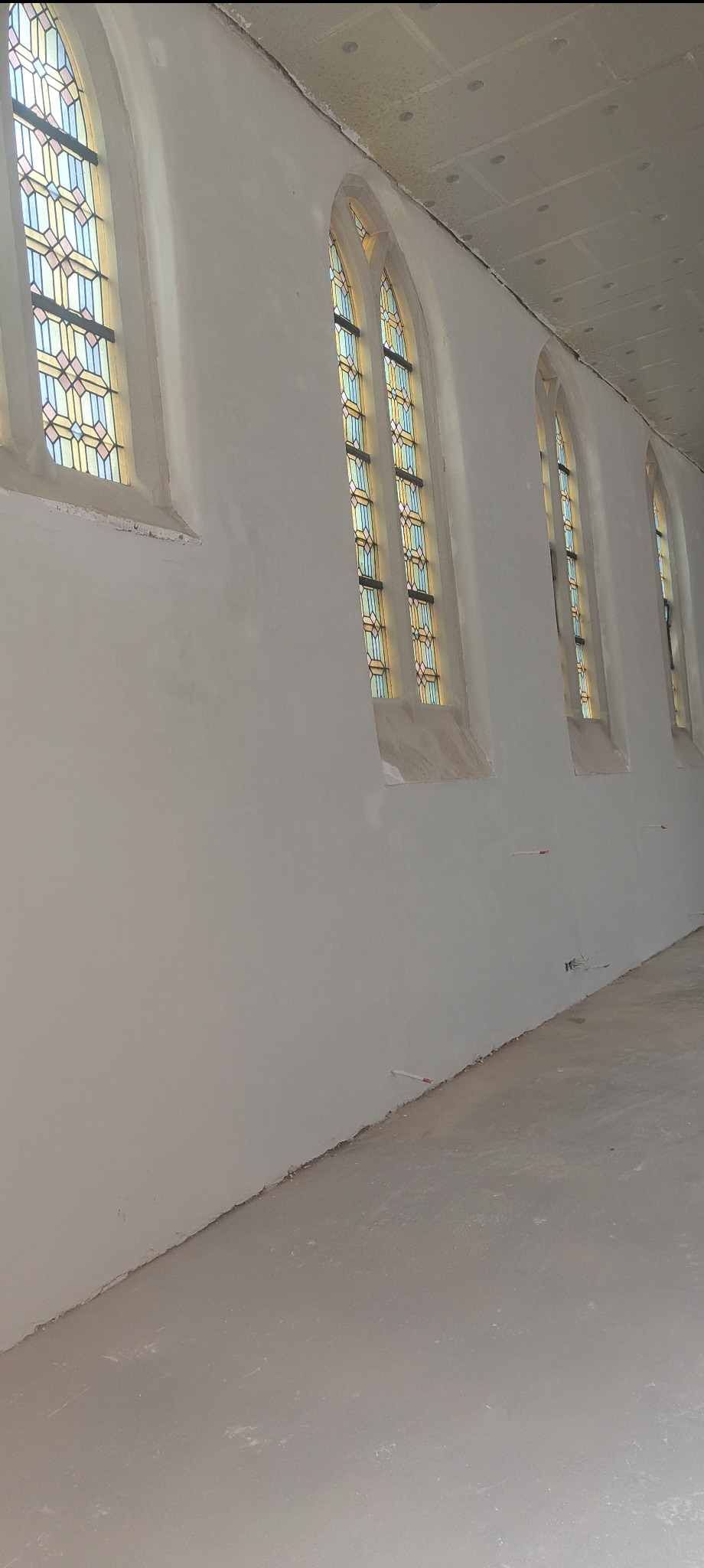Wnętrze po nałożeniu gładzi gipsowej w budynku sakralnym. Widoczne okna witrażowe i gładkie ściany. Świeżo położona gładź na ścianach i podłodze.