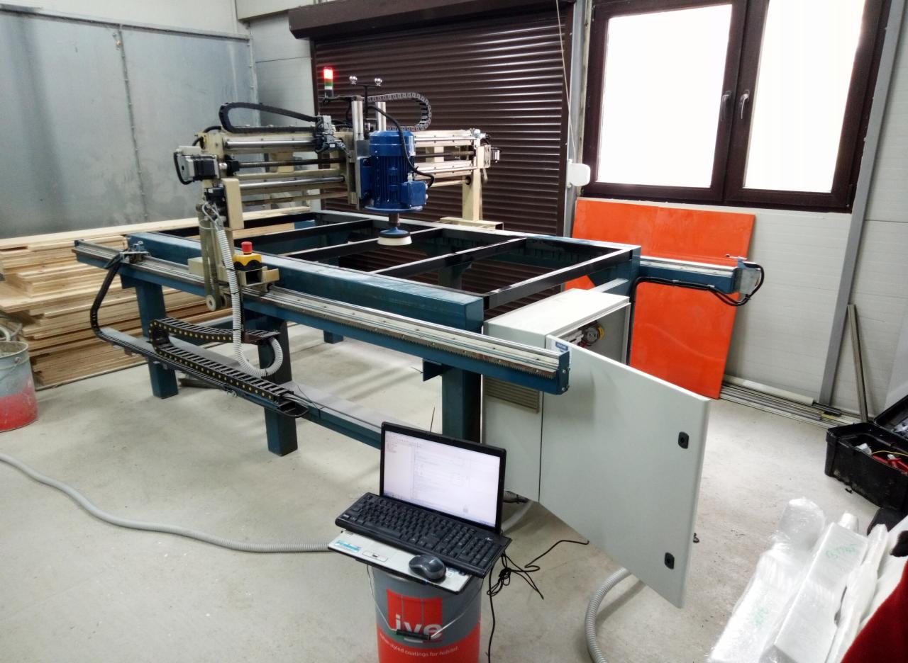 Maszyna polerska z automatyką, sterowana laptopem ustawionym na wiadrze z farbą, widoczna w hali produkcyjnej.