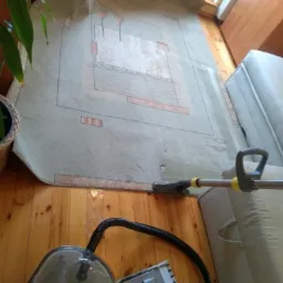 Fragment dywanu z geometrycznym wzorem czyszczony odkurzaczem piorącym, widoczne drewniane panele podłogowe i fragment sofy.