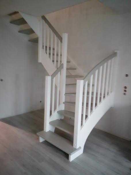 Jasne schody z białą balustradą z szarymi akcentami, widok od dołu, na tle szarej podłogi i białych ścian w surowym stanie.
