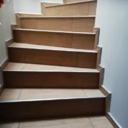 Schody wyłożone brązowymi płytkami imitującymi drewno, z metalowymi listwami na krawędziach stopni, widok z góry.