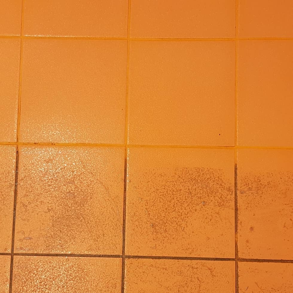 Pomarańczowe płytki podłogowe, częściowo zabrudzone, z ciemnymi fugami, widoczny efekt niedoczyszczonych plam.