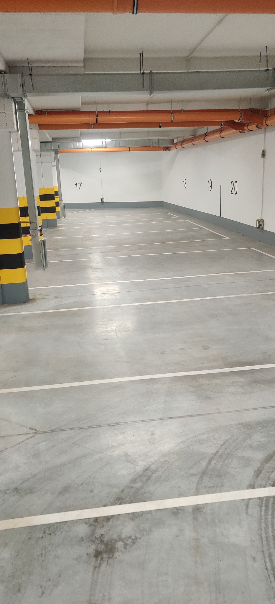 Puste, oświetlone miejsce parkingowe w garażu podziemnym z numerami miejsc 17, 18, 19 i 20 na ścianie.