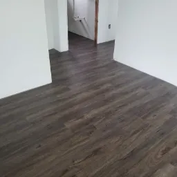 Ułożone ciemne panele podłogowe imitujące drewno w pomieszczeniu z białymi ścianami, widok z perspektywy podłogi.