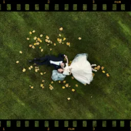 Para młoda leżąca na trawie, otoczona jesiennymi liśćmi, ujęcie z drona w ramce kliszy filmowej.