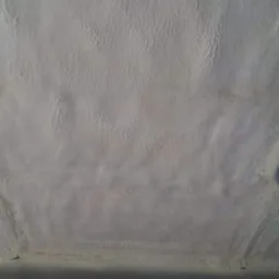 Szczegółowe ujęcie białej pianki PUR izolującej strop z widocznymi elementami mocującymi, ukazujące jej teksturę i równomierne rozprowadzenie.