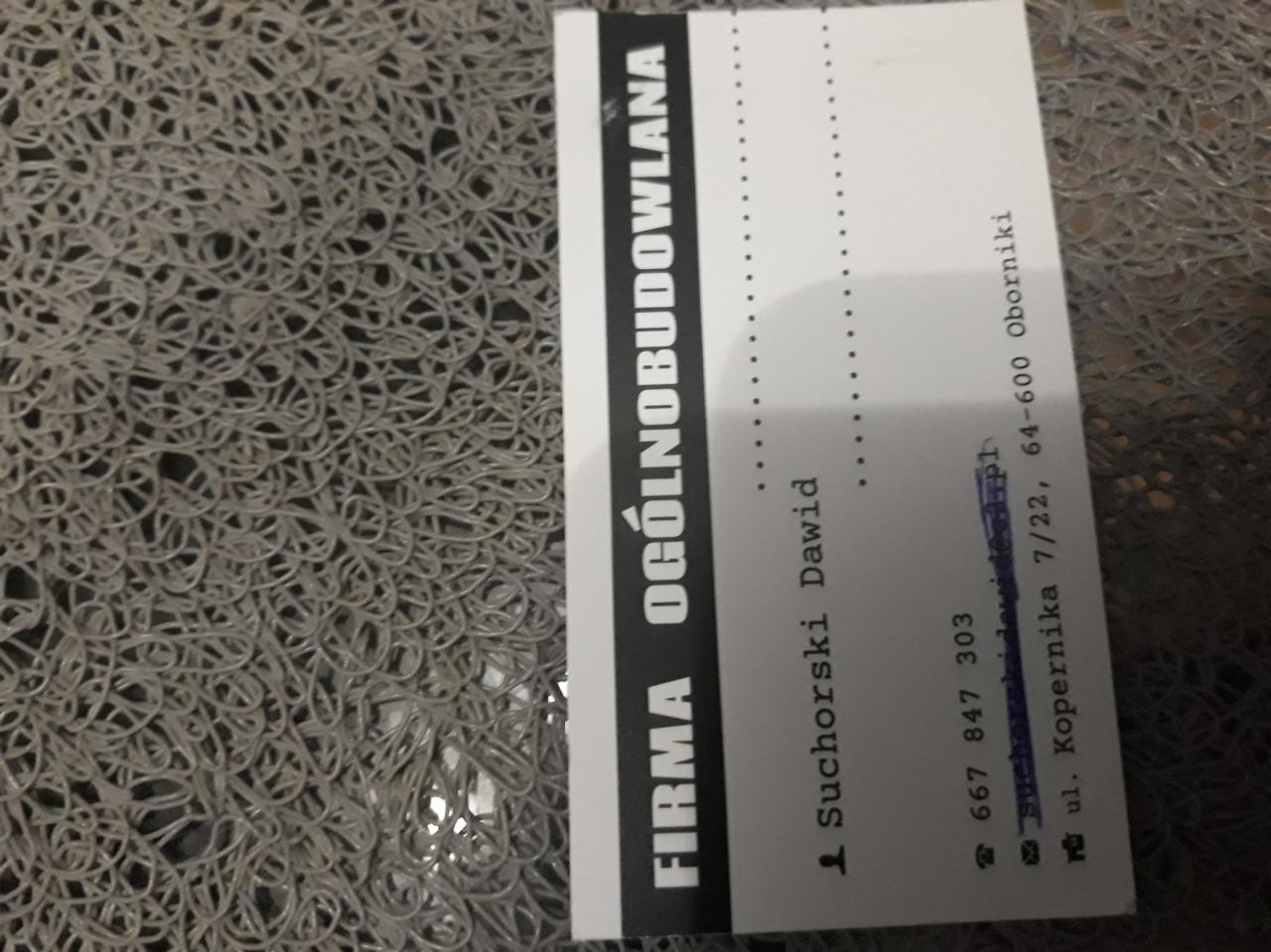 Wizytówka firmy ogólnobudowlanej Suchorski Dawid na szarej, teksturowanej powierzchni. Zawiera dane kontaktowe: numer telefonu i adres.