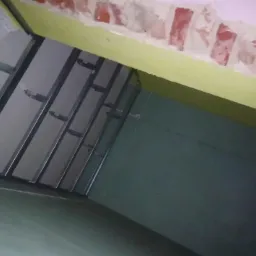 Montaż stelaża sufitu podwieszanego z płyt gipsowo-kartonowych na tle surowego muru i pomalowanej ściany.