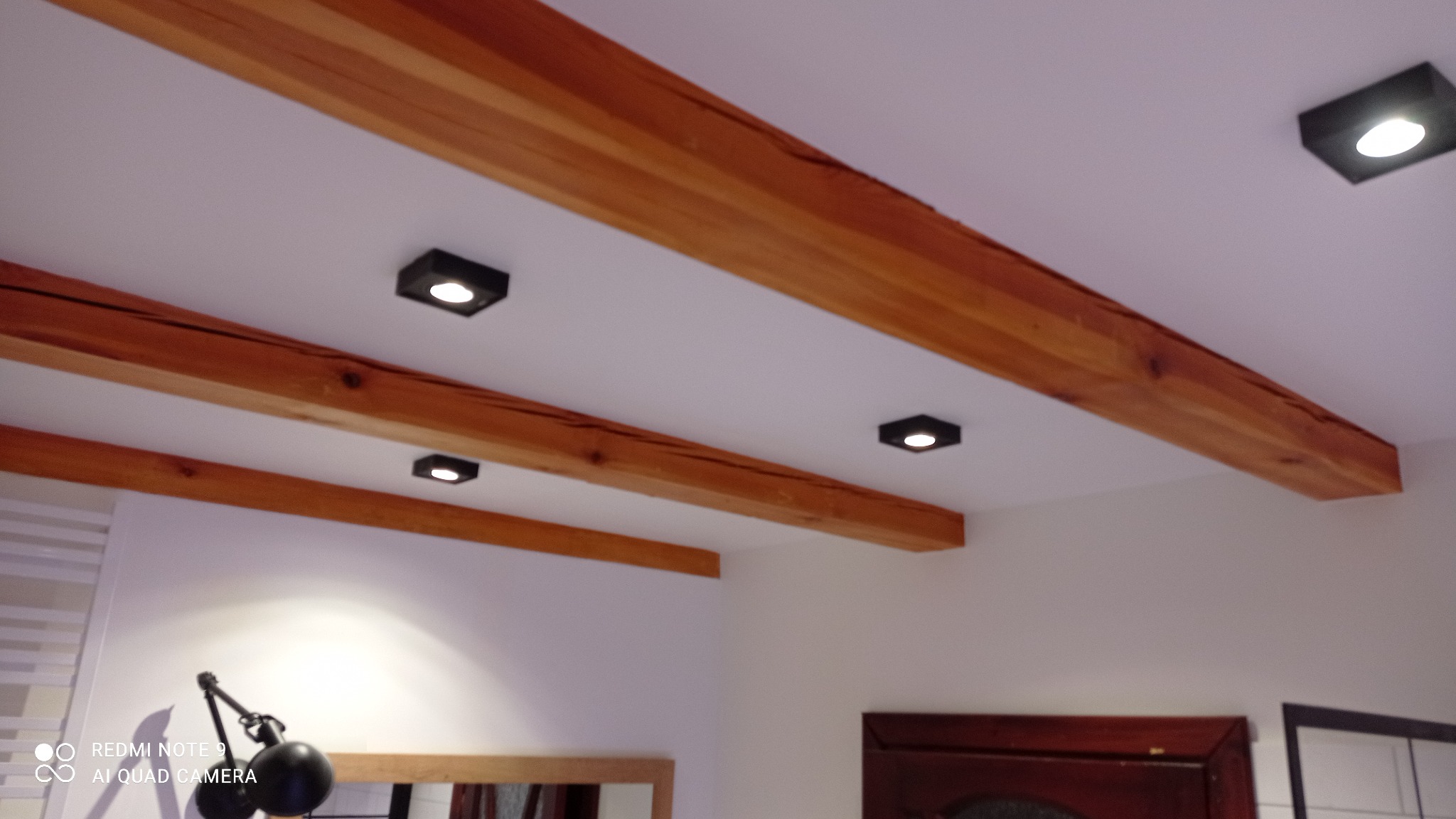 Drewniane belki stropowe z oświetleniem punktowym w mieszkaniu w Łodzi, widok z dołu.