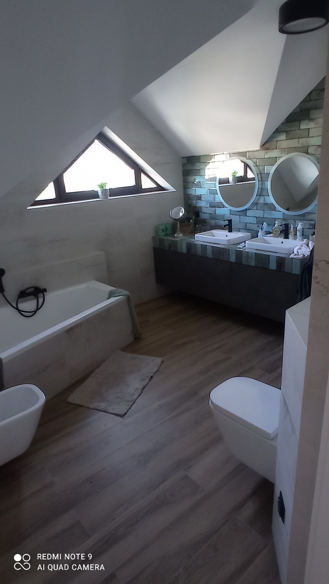 Nowoczesna łazienka na poddaszu z ukośnym oknem, dwiema okrągłymi umywalkami i wanną obudowaną marmurem.