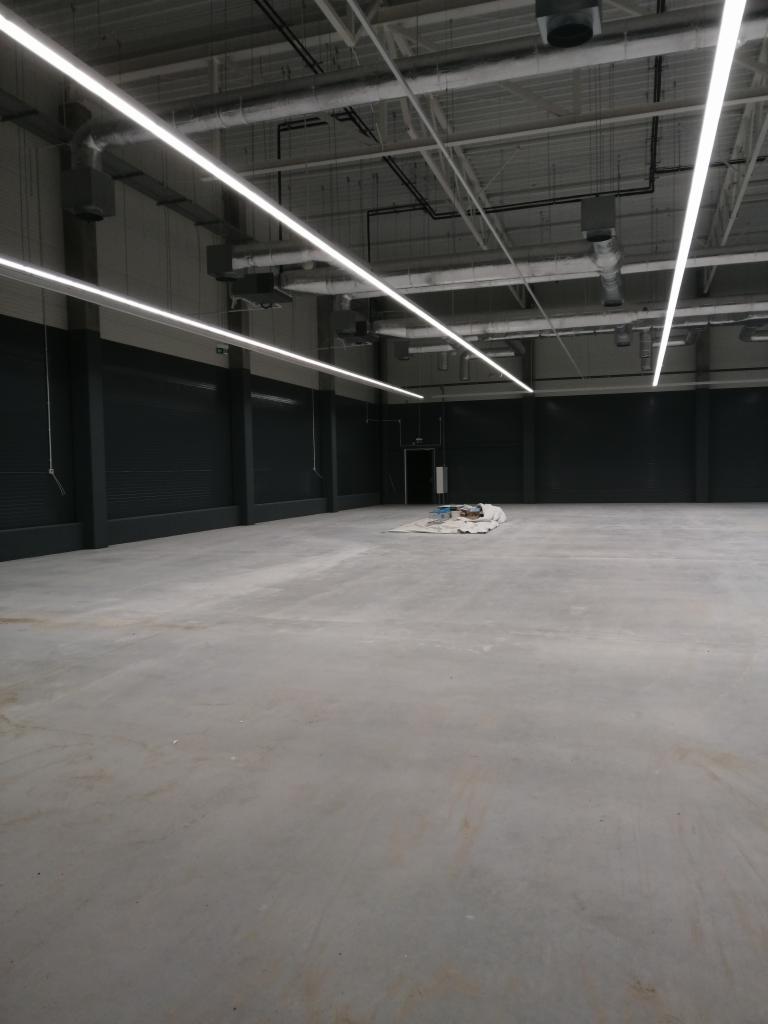 Przygotowane do prac wykończeniowych, surowe wnętrze hali w Żninie z widocznym betonowym podłożem i czarnymi ścianami. Na podłodze rozłożona plandeka zabezpieczająca.