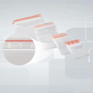 Cztery przezroczyste woreczki strunowe z czerwonym paskiem zamykającym, ułożone ukośnie w rosnącej wielkości, powiększony fragment woreczka z widocznymi symbolami recyklingu.