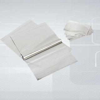 Błyszczące, srebrne arkusze folii aluminiowej ułożone w stosy na jasnym, gradientowym tle. Jeden stos rozłożony, ukazujący krawędź rolki folii.