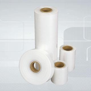 Różnej wielkości rolki przezroczystej folii stretch na tekturowych gilzach, ustawione na jasnoszarym tle.