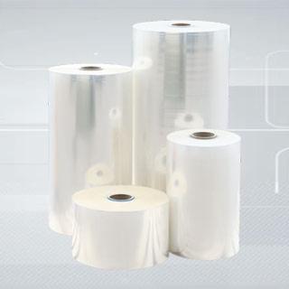 Cztery rolki przezroczystej folii termokurczliwej o różnych rozmiarach, ustawione na jasnoszarym tle z delikatnym gradientem.