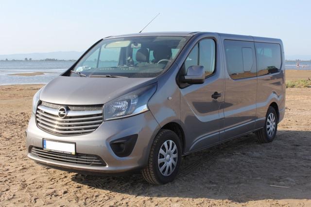 Szary Opel Vivaro na piaszczystej plaży z widokiem na morze w tle.