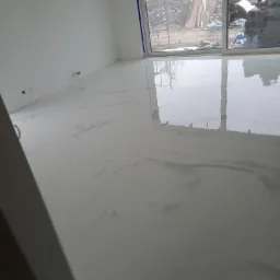 Biała, błyszcząca podłoga w jasnym pomieszczeniu z widokiem na plac budowy przez okno.