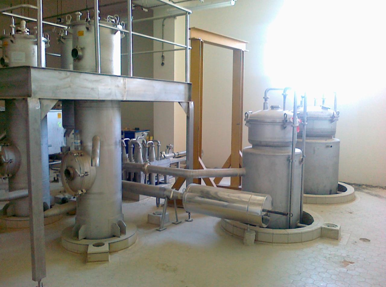 Metalowe zbiorniki ciśnieniowe połączone rurami w hali przemysłowej, z widoczną konstrukcją wsporczą i oświetleniem górnym.