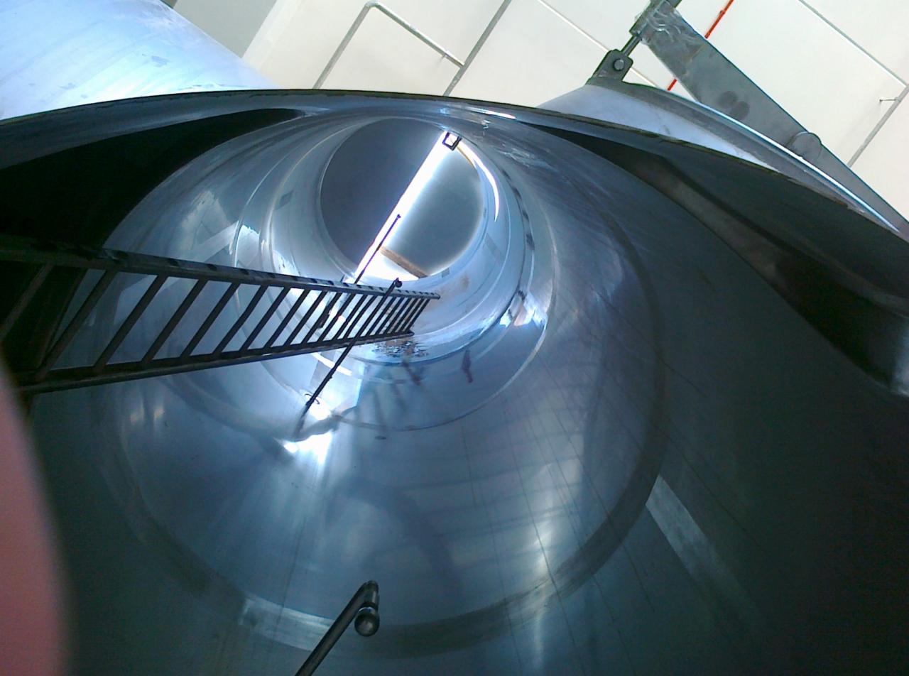 Wnętrze metalowego silosu z zamontowaną drabiną, widok z dołu w kierunku otworu z jasnym światłem.