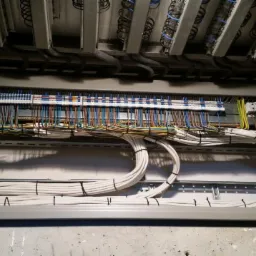 Rozdzielnica elektryczna z precyzyjnie ułożonymi przewodami o różnych kolorach, uporządkowane kable białe spięte czarnymi opaskami, widoczne listwy montażowe i elementy złączne.