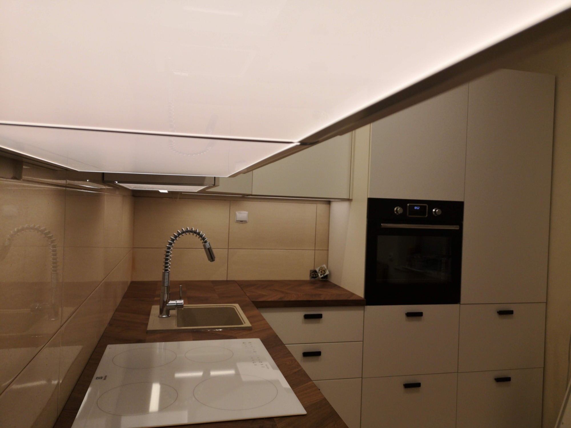 Nowoczesna kuchnia IKEA z drewnianym blatem, białymi szafkami i płytą indukcyjną, oświetleniem sufitowym LED i chromowaną baterią kuchenną.