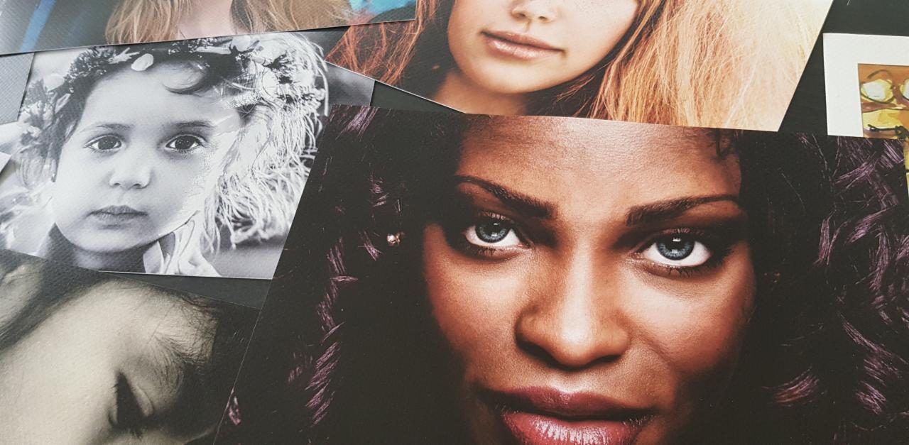 Stos wydrukowanych fotografii portretowych o różnej tematyce i stylistyce, w tym zbliżenie na twarz kobiety z intensywnym spojrzeniem.