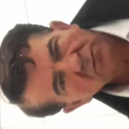 Portret mężczyzny w białej koszuli i marynarce, sfotografowany z bliska, z widocznymi detalami twarzy.