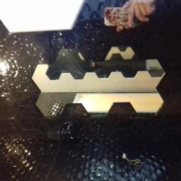 DARMI REMONTY I WYKOŃCZENIA WNĘTRZ - Układanie heksagonalnych płytek: czarne płytki z tłoczonym wzorem i białe akcenty, widoczne przewody elektryczne w dolnej części kadru, odbicie telefonu w powierzchni płytek.