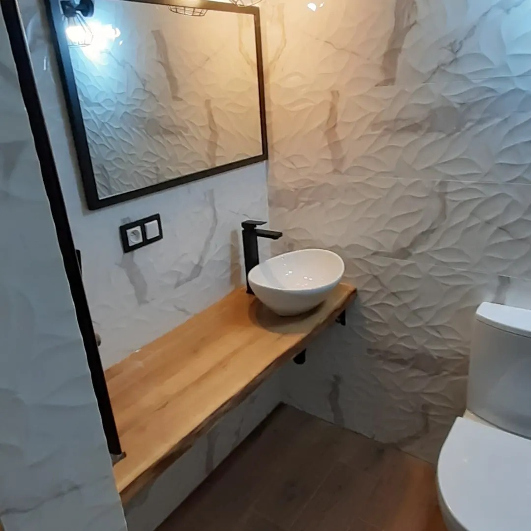 Nowoczesna łazienka z umywalką nablatową na blacie z litego drewna, czarna bateria, lustro w czarnej ramie i dekoracyjne płytki ścienne o falistej strukturze.