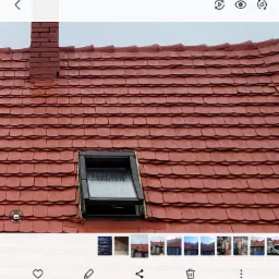 Czerwona dachówka karpiówka z kominem z cegły i oknem dachowym. Widok z dołu na skośny dach. Detal pokrycia dachowego po renowacji.