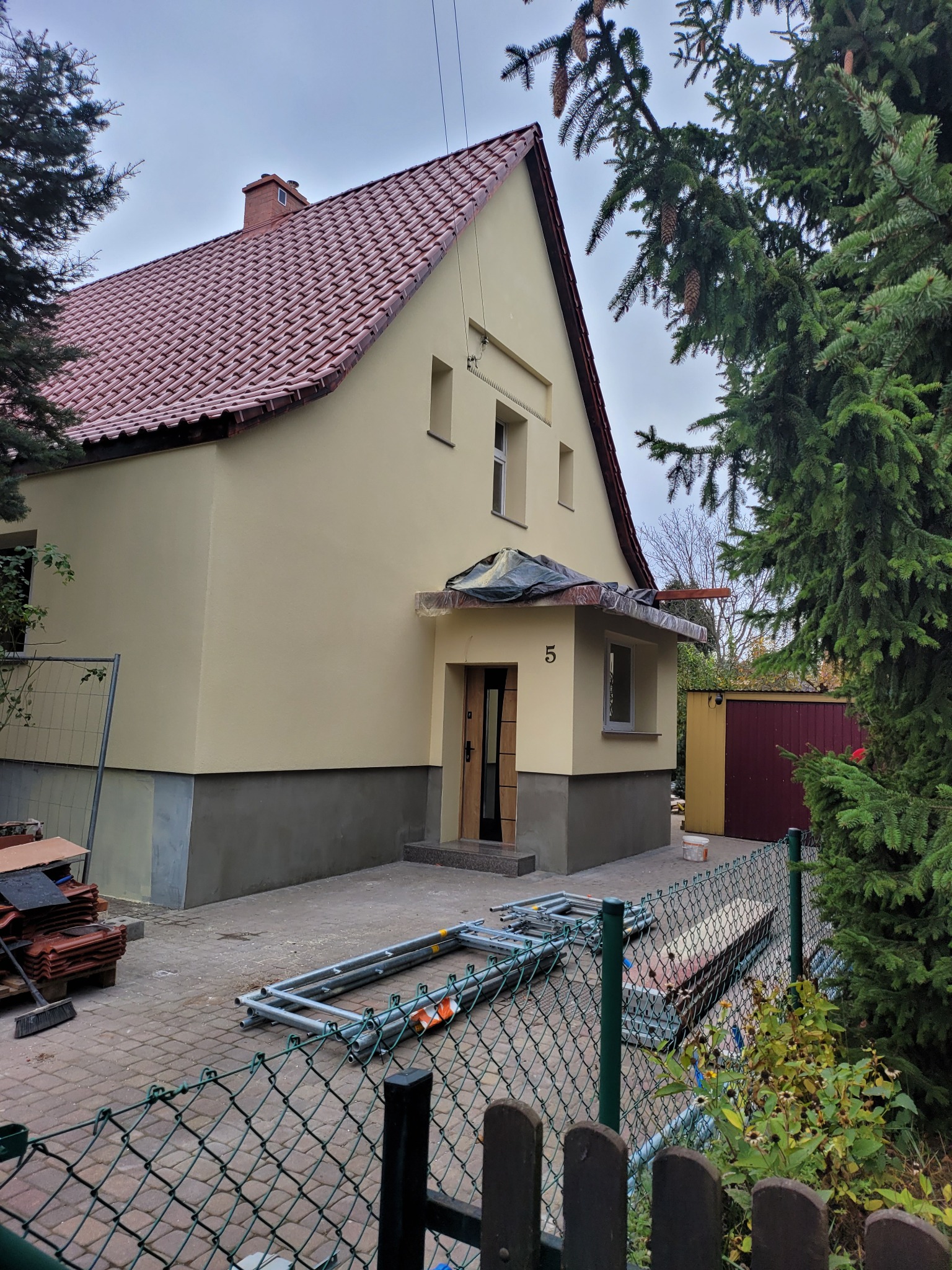 Ocieplona elewacja budynku jednorodzinnego w trakcie prac wykończeniowych, widoczne rusztowania i materiały budowlane, nowa dachówka ceramiczna.