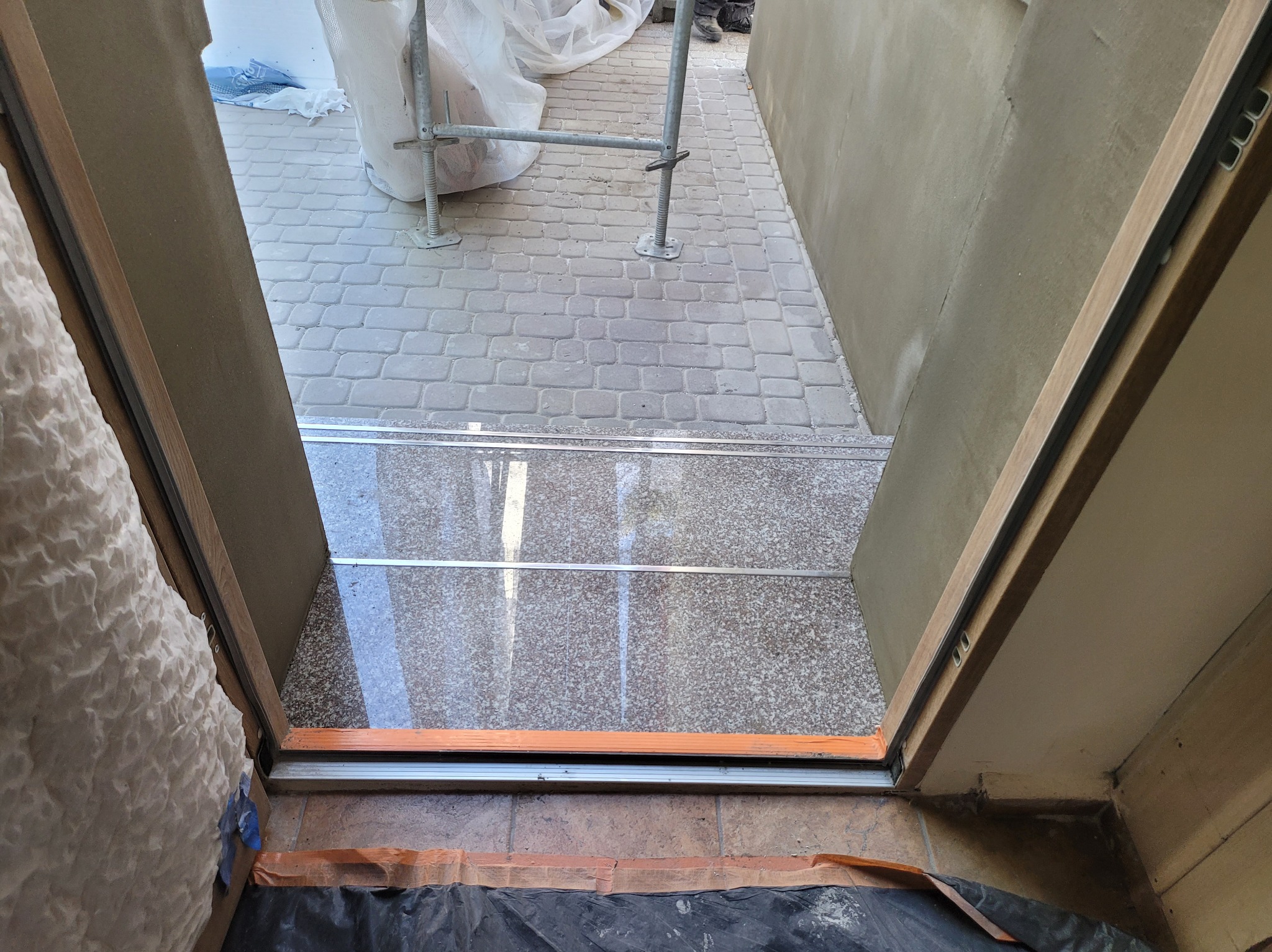 Przygotowanie do ocieplenia elewacji: widok od wewnątrz przez otwór okienny na zewnątrz, gdzie stoi rusztowanie i widać fragment otynkowanej ściany.