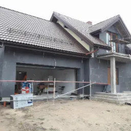 Dom jednorodzinny w trakcie ocieplania elewacji styropianem grafitowym, widoczne rusztowania, worki z zaprawą i paczki styropianu EPS S 033.