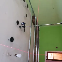 Montaż stelażu pod płytę karton gips z użyciem poziomicy laserowej, widoczne profile, uchwyty ES i wiązka lasera na ścianie z niedokończonym oświetleniem.