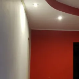 Pomieszczenie po malowaniu z dekoracyjnym, czerwonym elementem sufitu podwieszanego z oświetleniem punktowym, ściany białe i czerwone, podłoga drewniana.
