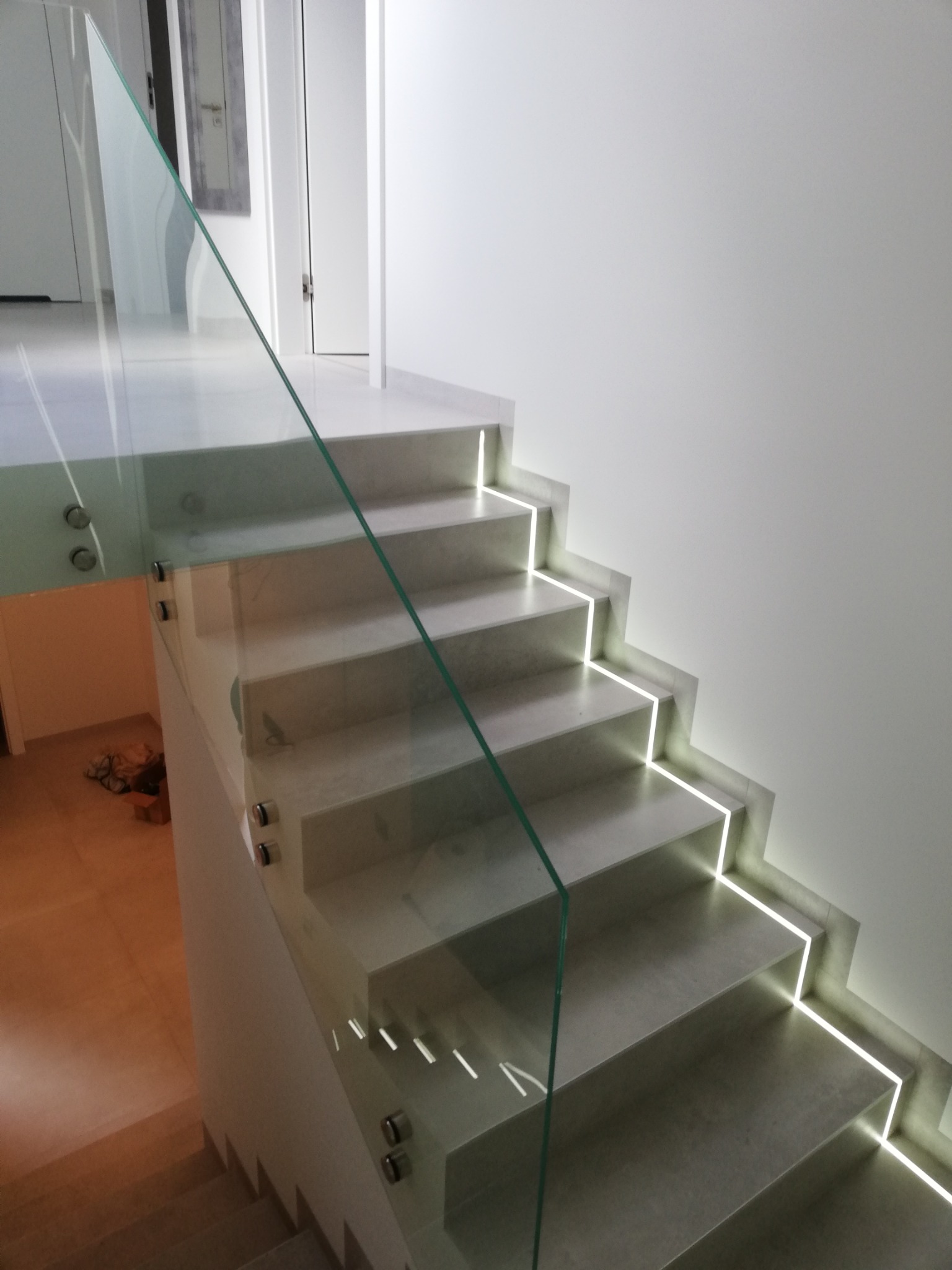 Szklana balustrada schodowa z podświetleniem LED wzdłuż stopni, mocowana punktowo, widok z dołu.