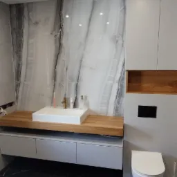 Nowoczesna łazienka z marmurową ścianą, drewnianym blatem pod umywalką i czarną podłogą z białym wzorem. Minimalistyczny design, oświetlenie punktowe.