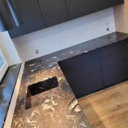 Czarny blat kuchenny z marmurkowym wzorem, zintegrowany z czarnym zlewem i szafkami w nowoczesnej kuchni z drewnianą podłogą.