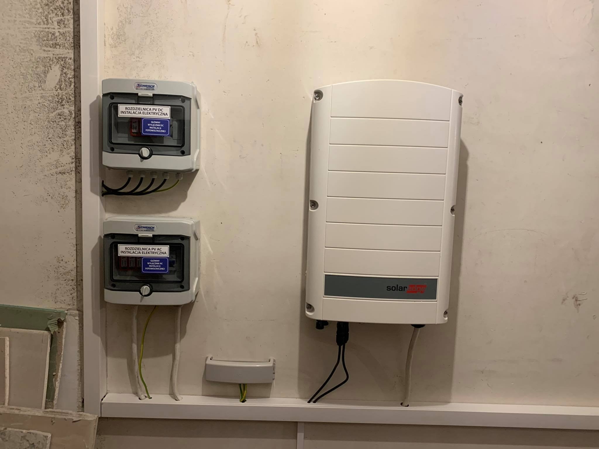 Dwa rozdzielnice PV DC/AC firmy Schrack oraz inwerter SolarEdge zamontowane na ścianie z widocznymi przewodami elektrycznymi.
