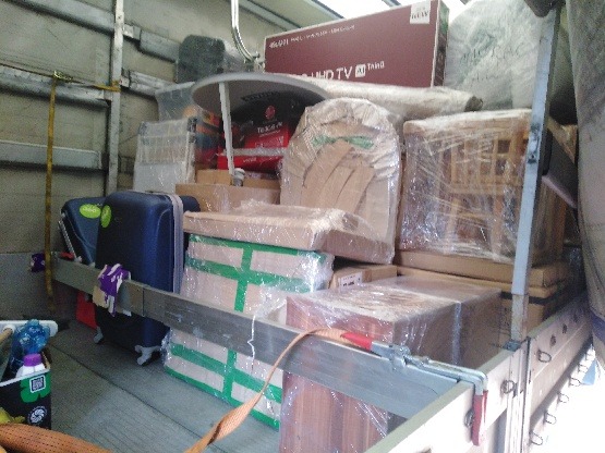 Wnętrze samochodu dostawczego wypełnione po brzegi zapakowanymi meblami, kartonami i walizkami podczas transportu, zabezpieczone pasami.