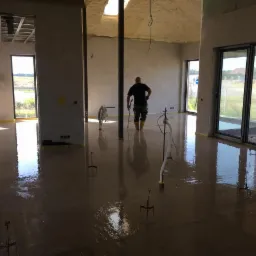 Wylewka samopoziomująca w trakcie realizacji w nowym domu w Poznaniu, widoczny pracownik w gumowych butach i narzędzia do rozprowadzania masy.