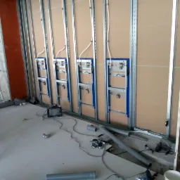 Wewnętrzna instalacja sanitarna w trakcie montażu: stelaże podtynkowe WC zamocowane do metalowego szkieletu ściany działowej, widoczne rury i przewody, surowy stan wykończenia.