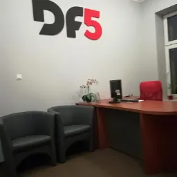 Biuro z dwoma szarymi fotelami, biurkiem z komputerem i czerwonym krzesłem oraz logo firmy 'Df5' na ścianie.