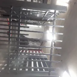 Metalowa konstrukcja kraty z poziomymi prętami, szara, widok z dołu na górę, oświetlenie z góry.