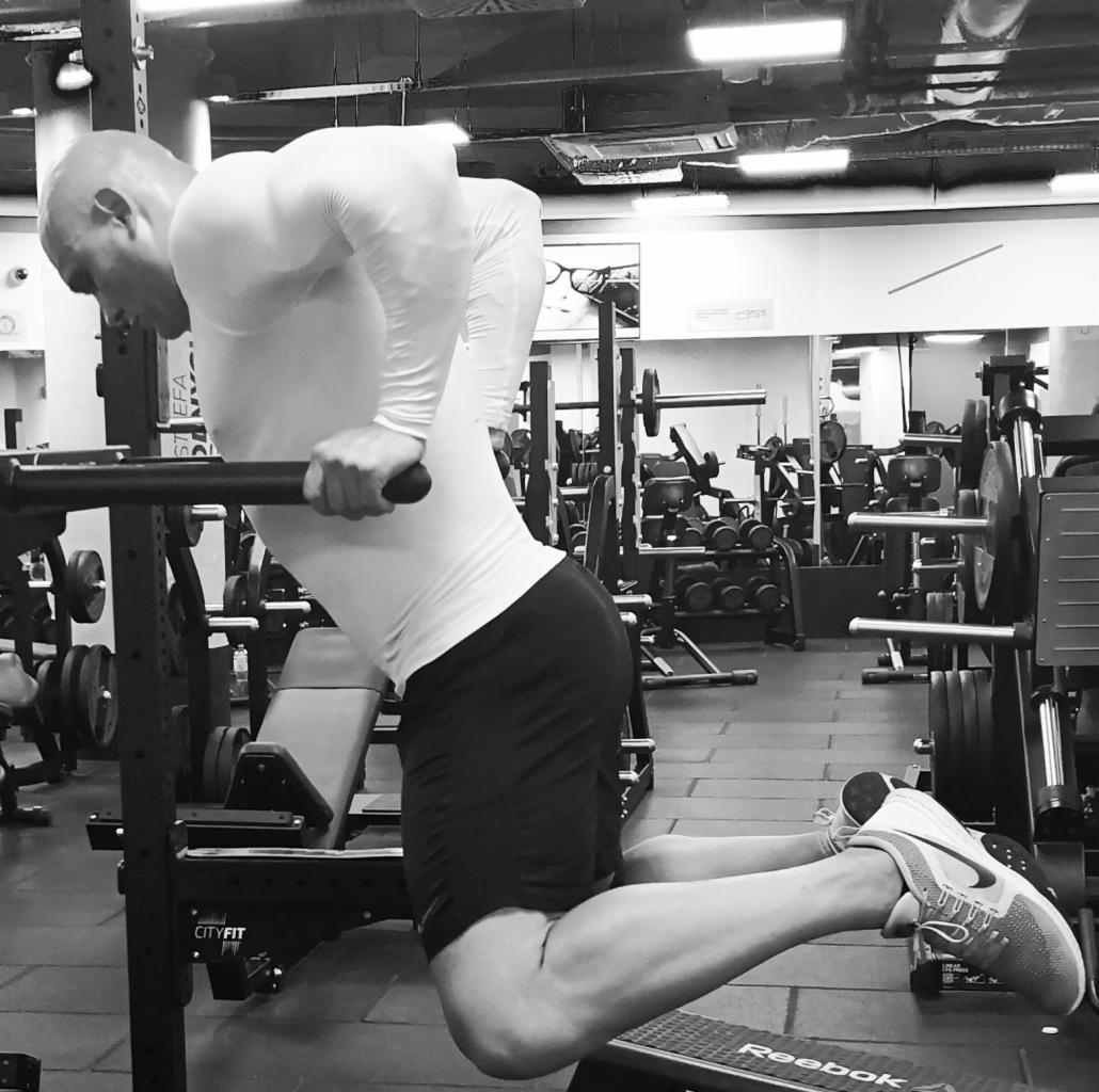 Mężczyzna wykonuje ćwiczenie na poręczach w siłowni, widoczne obciążenia, sprzęt do ćwiczeń, tło rozmyte, zdjęcie czarno-białe.