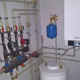 Kompletna instalacja grzewcza z piecem gazowym Viessmann, zbiornikiem, pompami obiegowymi i rozbudowanym systemem rur w pomieszczeniu kotłowni.