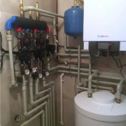 Węzeł rozdzielaczowy z pompami obiegowymi, zbiornik wyrównawczy, zasobnik CWU i piec gazowy Viessmann w kotłowni wykończonej płytkami ceramicznymi.