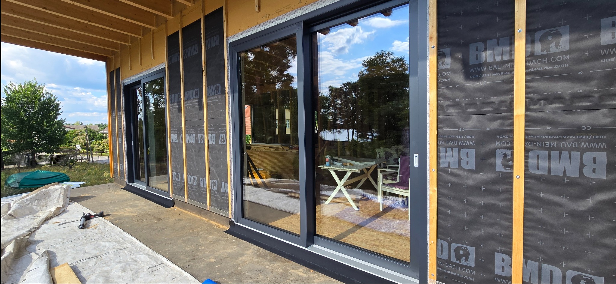 Montaż przesuwnych okien tarasowych z czarnymi ramami w nowo budowanym domu. Widoczne detale konstrukcyjne i izolacja.